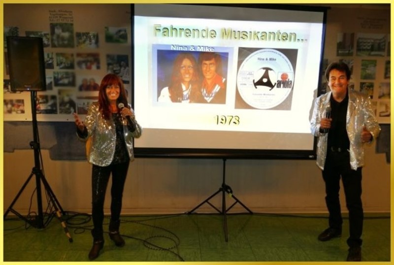 Die Schlagerpiratin steht links und Schatzi rechts neben der Leinwand beim Mitsingkonzert.