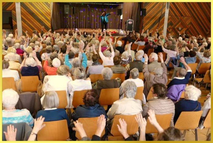 Gro�e Halle mit Senioren besetzt. Schlagers�ngerin auf der B�hne. H�nde hoch.
