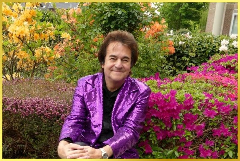 Schatzi Ian sitzt mit Glitzerjacke umgeben von sch�nen Blumen.