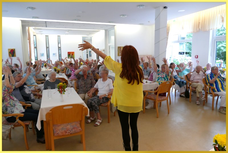 Gro�er Saal mit Senioren. Alle winken, die Schlagerpiratin singt.