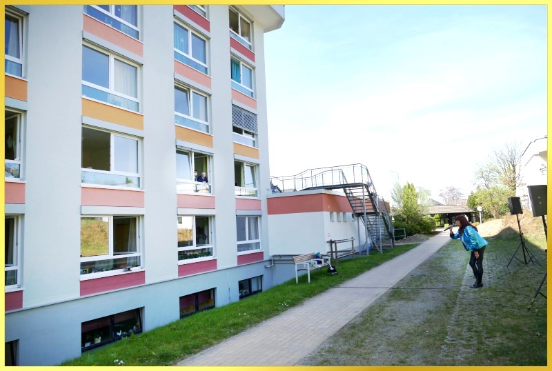 Schlagerpiratin steht vor Geb�ude mit offenen Fenstern und singt.