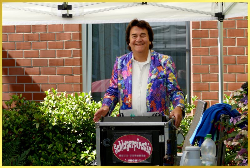 Schatzi Ian lacht hinter dem Pult in die Kamera.