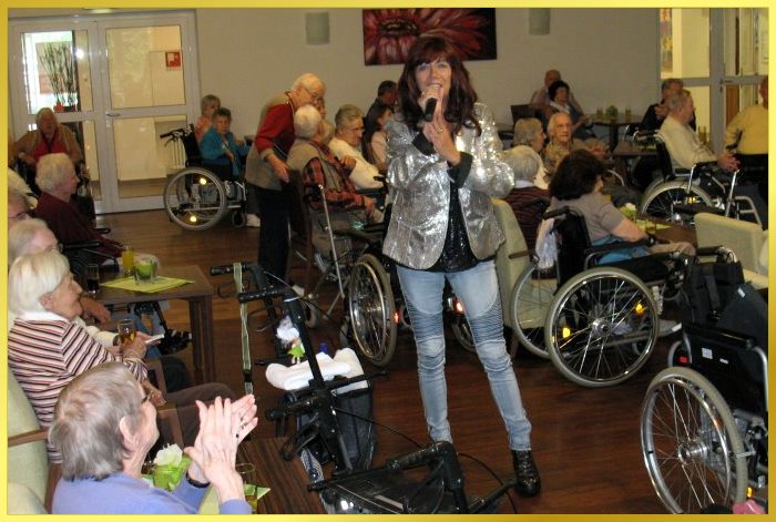 S�ngerin zwischen Rollst�hlen singt alte Schlager f�r die Senioren.