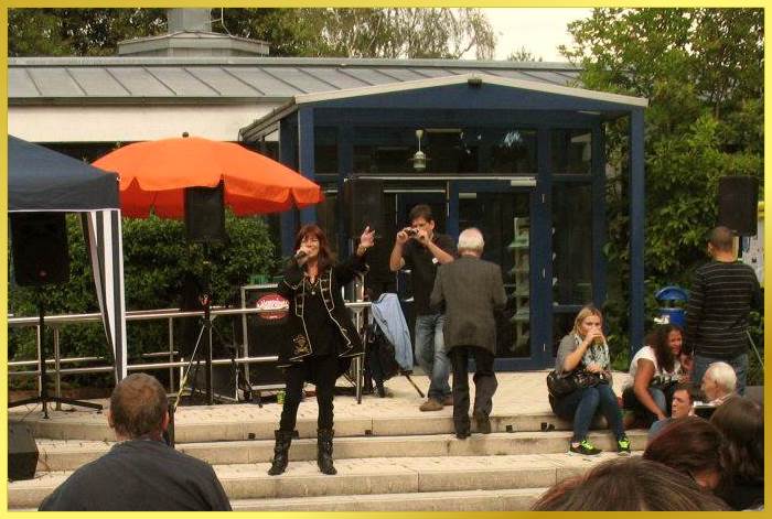 Schlagers�ngerin singt Open Air auf einer Steintreppe vor einer Aktionshalle.