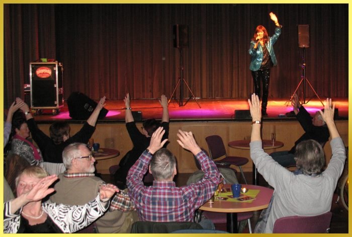 Schlagerpiratin steht auf gro�er B�hne im Rathaussaal. Publikum winkt.