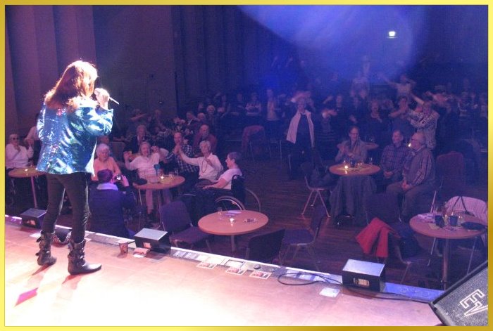 Hellbeleuchtete B�hne mit S�ngerin. Viel Publikum im Saal.