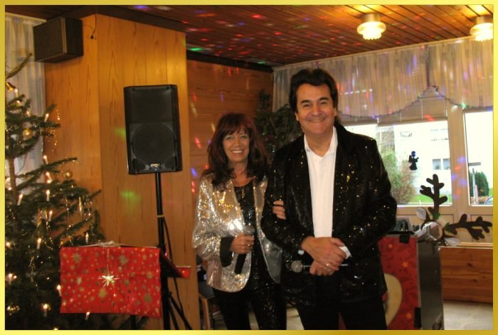 Schatzi und Marina neben Weihnachtsbaum. Lachen in die Kamera.