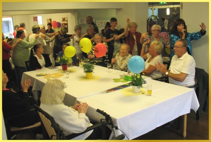 Polonaise mit Marina im t�rkiesem Glitzer-Look. Bewohner laufen fr�hlich winkend hinterher.