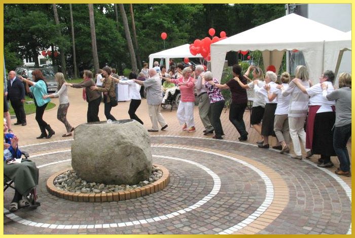 Riesen Polonaise um einen Springbrunnen! Dahinter Zelte und rote Luftballons.
