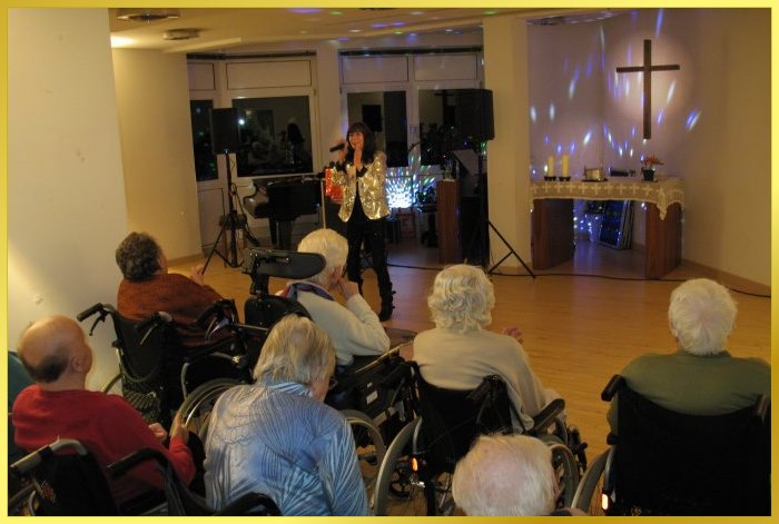 Schlagerpiratin singt Weihnachtslieder f�r behinderte Senioren. Beleuchtetes Jesuskreuz an der Wand.