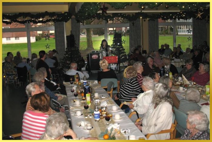 Riesig groer Saal, vollbesetzt mit Senioren. Schlagersngerin zwischen 2 Weihnachtsbumen singt.